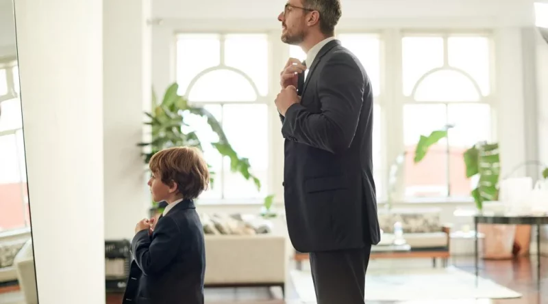 Papa qui ajuste sa cravate devant un miroir avec son enfant en costume qui fait la même chose devant lui