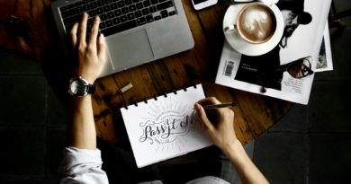 Personne travaillant sur un bureau avec un ordinateur portable, un carnet de croquis, un smartphone et une tasse de café.