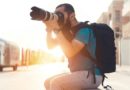 Photographe assis sur un banc, prenant une photo avec un appareil photo professionnel en pleine lumière du jour.