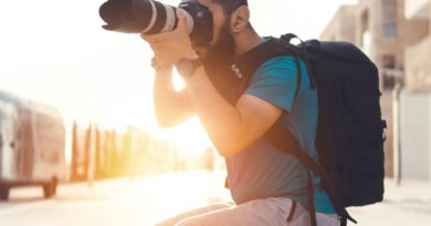 Photographe assis sur un banc, prenant une photo avec un appareil photo professionnel en pleine lumière du jour.
