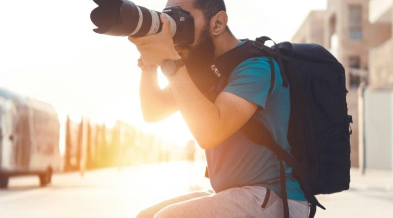 Photographe assis sur un banc, prenant une photo avec un appareil photo professionnel en pleine lumière du jour.