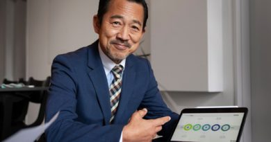 Homme en costume bleu souriant et pointant un graphique circulaire affiché sur une tablette lors d’une présentation professionnelle.