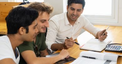 Trois hommes discutent à une table avec des documents et une tablette