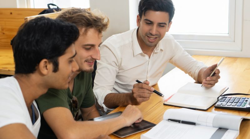 Trois hommes discutent à une table avec des documents et une tablette