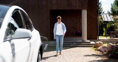 Homme marchant devant une maison en bois avec une voiture blanche en charge.