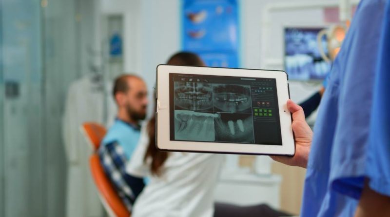 Dentiste tenant une tablette avec une radiographie, patient assis sur un fauteuil
