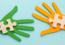 Deux mains découpées en papier, l’une verte et l’autre orange, tenant chacune une pièce de puzzle en bois.