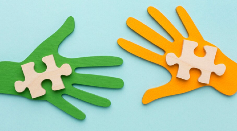 Deux mains découpées en papier, l’une verte et l’autre orange, tenant chacune une pièce de puzzle en bois.