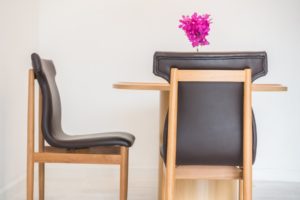 Deux chaises en bois avec assise en cuir autour d’une table, décorées d’un vase de fleurs roses.