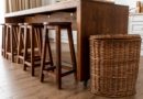 Tabourets en bois alignés sous une table avec un grand panier en osier à côté.