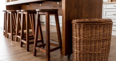 Tabourets en bois alignés sous une table avec un grand panier en osier à côté.