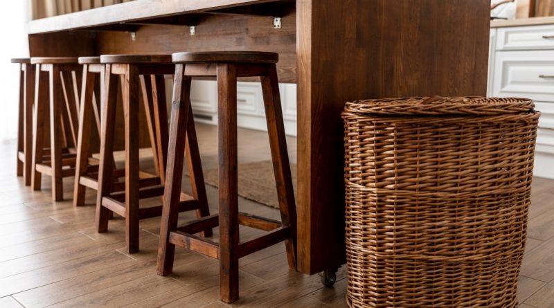 Tabourets en bois alignés sous une table avec un grand panier en osier à côté.