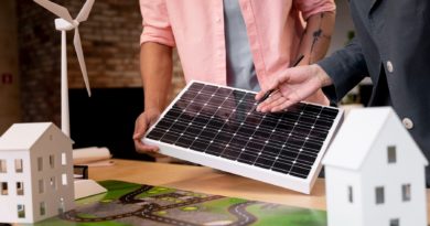 Deux personnes examinent un panneau solaire près de maquettes de maisons et d’une éolienne, illustrant un projet d’énergie renouvelable