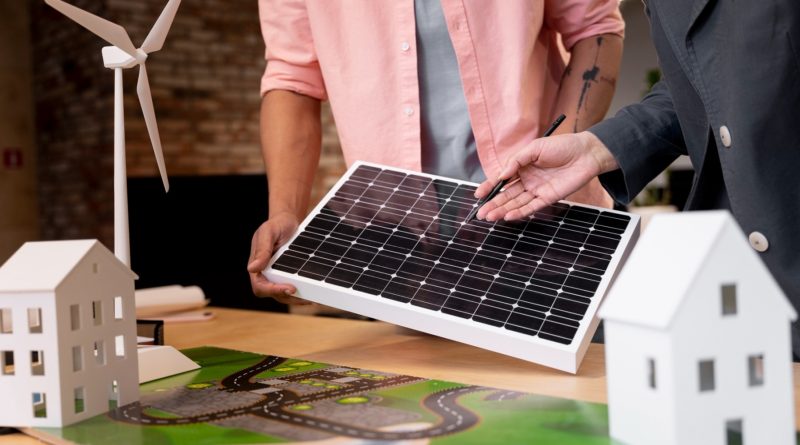 Deux personnes examinent un panneau solaire près de maquettes de maisons et d’une éolienne, illustrant un projet d’énergie renouvelable