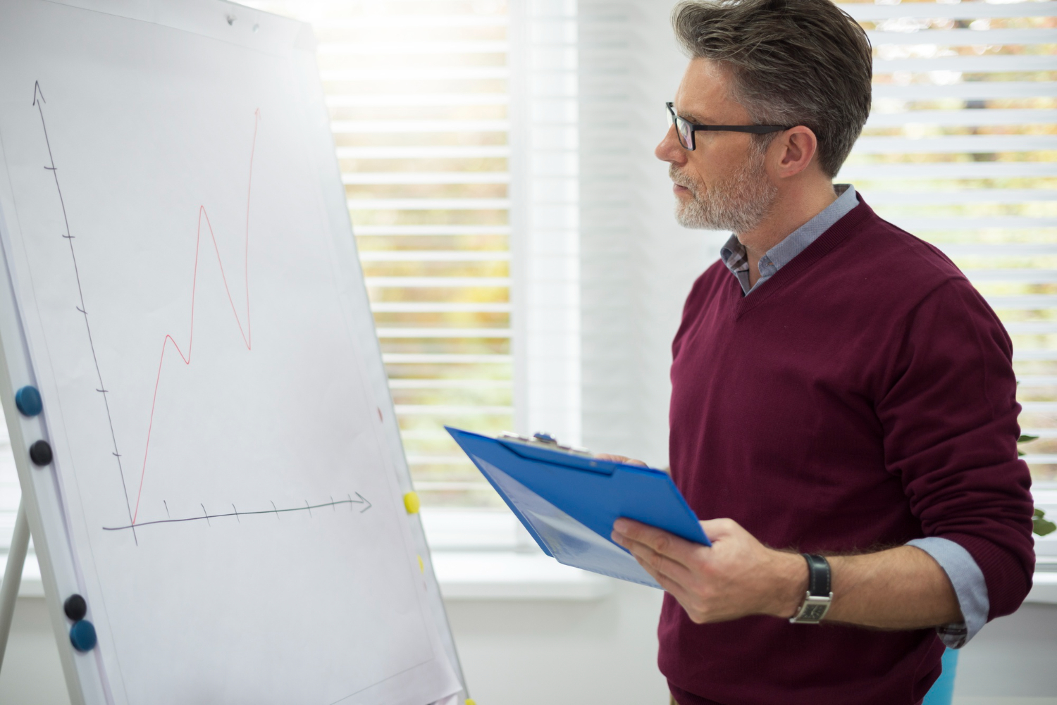 Un homme regarde un graphique sur un tableau blanc et tient un classeur bleu.
