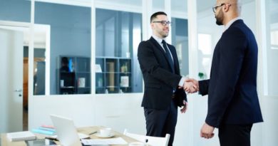 Deux hommes en costume se serrent la main dans un bureau lumineux, avec une table et un ordinateur devant eux