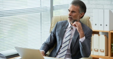 Un homme d'affaires mûr et réfléchi est assis à son bureau devant un ordinateur portable, tenant ses lunettes à la main