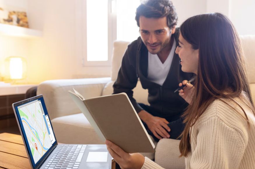 Une femme tient un carnet de notes et un stylo tout en regardant l'écran d'un ordinateur portable