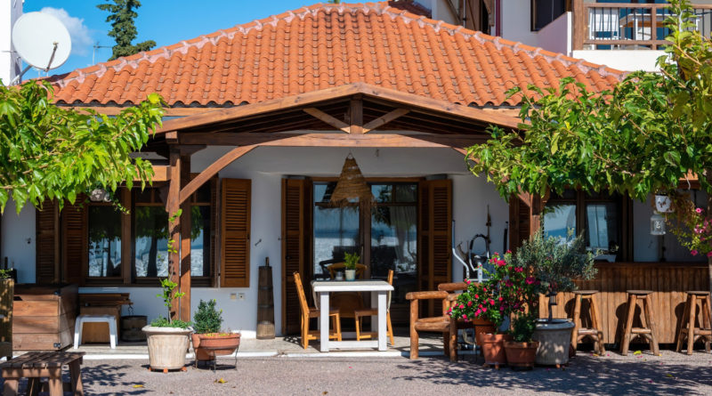 Une terrasse de maison avec un toit en tuiles, des meubles en bois et de nombreuses plantes en pot