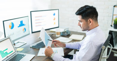 un homme travaille à son bureau devant plusieurs écrans affichant des graphiques financiers et des statistiques