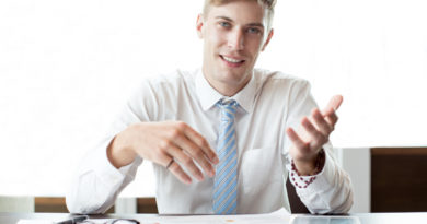 Un jeune consultant souriant en chemise blanche et cravate bleue explique des documents posés sur son bureau