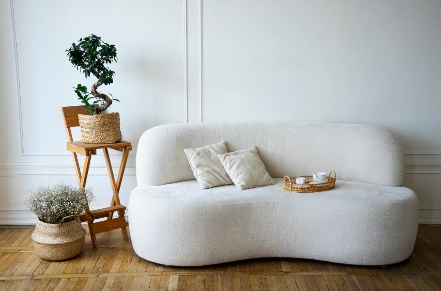 un canapé blanc arrondi, un parquet en bois et des plantes décoratives dans des paniers en osier