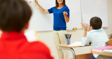 Une enseignante en haut bleu explique une équation algébrique au tableau blanc devant ses élèves en classe