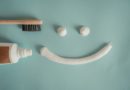 une brosse à dents en bambou et un tube de dentifrice à gauche. Au centre, trois noisettes de dentifrice blanc sous forme d'un visage souriant