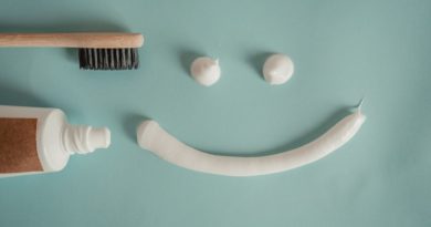 une brosse à dents en bambou et un tube de dentifrice à gauche. Au centre, trois noisettes de dentifrice blanc sous forme d'un visage souriant
