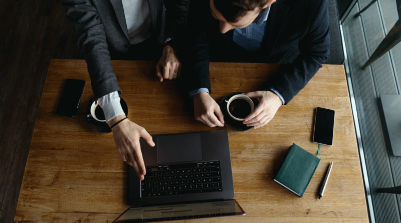 Vue de dessus de deux collaborateurs échangeant autour d'un ordinateur et d'un café