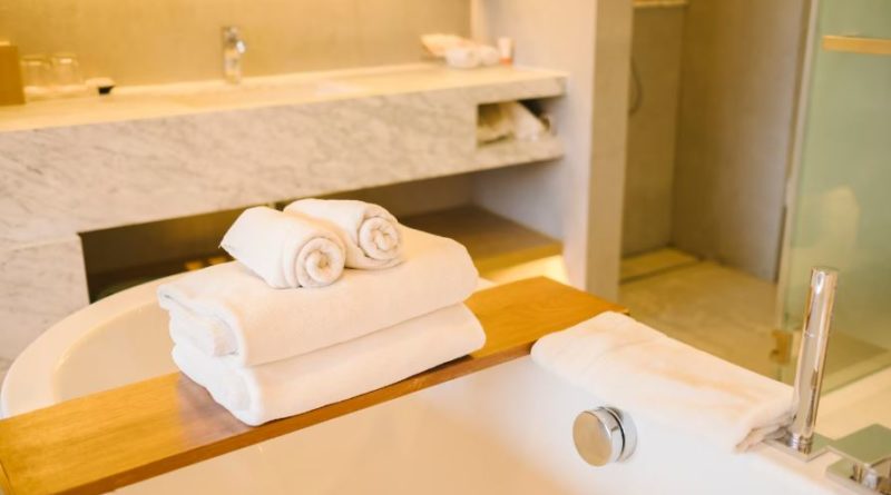 Une pile de serviettes de bain blanches moelleuses posée sur un pont de baignoire en bois, dans une salle de bain de luxe moderne.