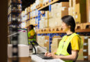 Un opérateur logistique asiatique en gilet jaune tape sur son clavier face à son écran de contrôle dans un entrepôt de stockage.