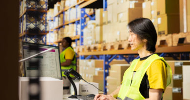 Un opérateur logistique asiatique en gilet jaune tape sur son clavier face à son écran de contrôle dans un entrepôt de stockage.