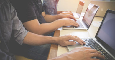 les mains de plusieurs personnes assises en ligne, en train de travailler activement sur leurs ordinateurs portables alignés sur une table de bureau