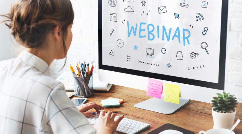 Une femme de dos travaille sur un ordinateur de bureau affichant le mot « WEBINAR » entouré d'illustrations liées à la communication numérique.