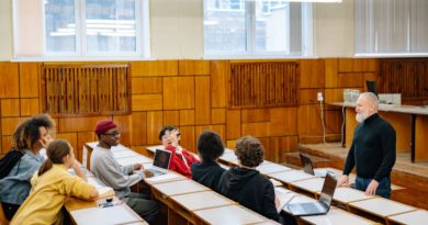 un enseignant senior à la barbe blanche debout face à un groupe d'étudiants multiculturels attentifs lors d'un cours dispensé dans un amphithéâtre universitaire.